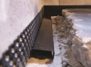 photo of DRY-UP™ water tunnel installed in a wet basement - a metal half-tube sitting on the footing next to the dimple board
