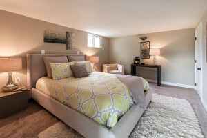 photo of a bedroom with a bed with a yellow patterned bedspread in a finished basement that is waterproofed