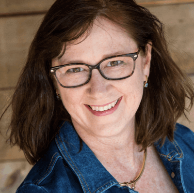 photo of Becky Dean wearing a jean jacket, glasses, with brown hair.
